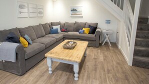 Ein Wohnzimmer mit einem grauen Ecksofa, einem Holztisch und einer Treppe.