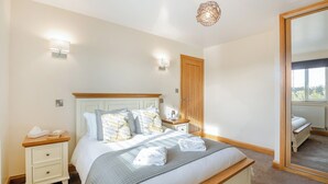 A bedroom with a bed, bedside tables, a mirror, and a window. - Manawydan Cottage - UKC6124 (Pentraeth)
