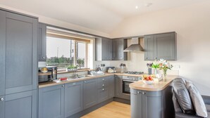 A modern kitchen with grey cabinets, a wooden countertop, a built-in oven, and a window providing natural light. - Manawydan Cottage - UKC6124 (Pentraeth)