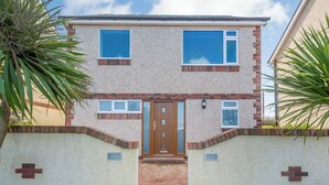 A two-story house with a brick facade, a central wooden door, and a small front garden. - Manawydan Cottage - UKC6124 (Pentraeth)