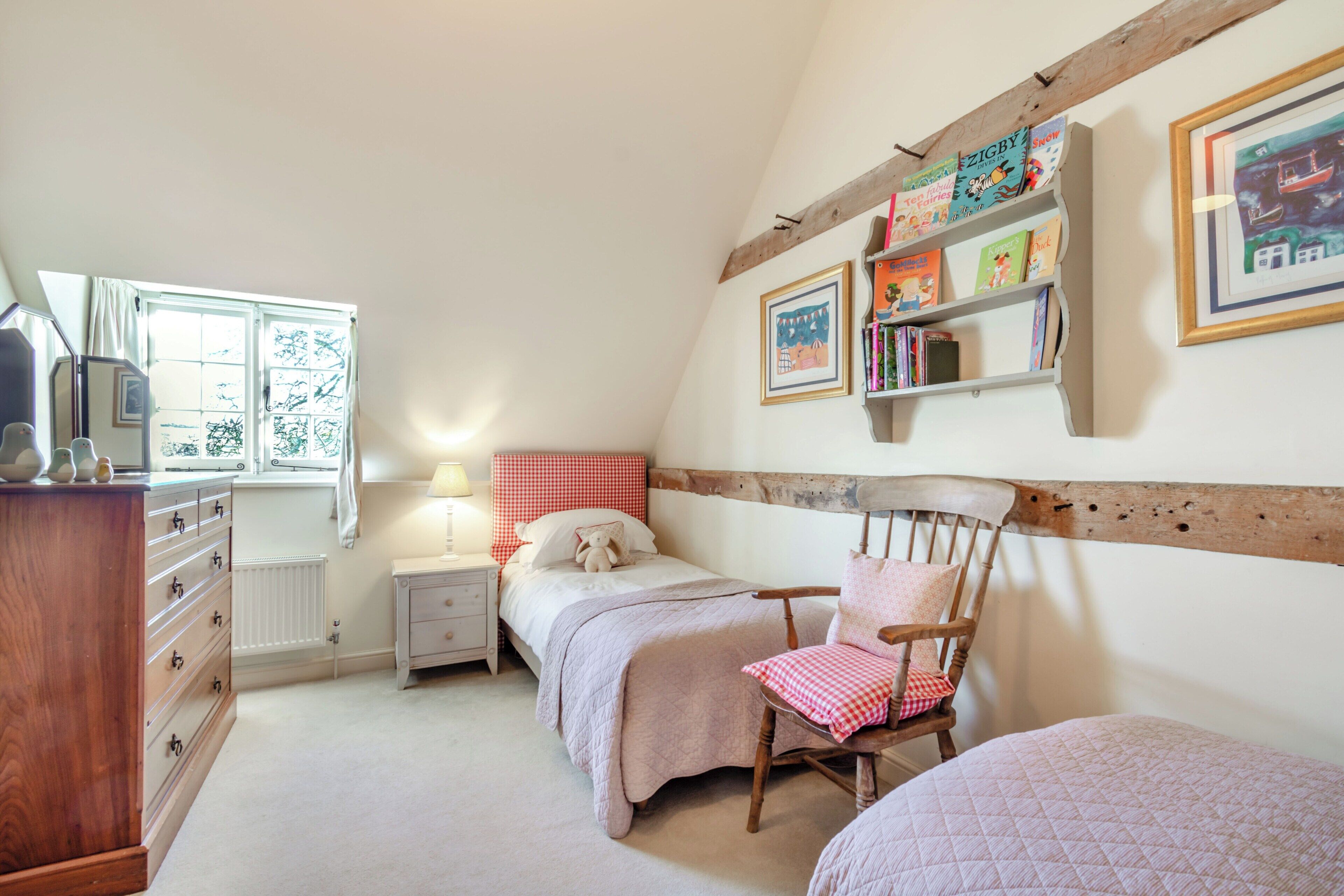 Une chambre avec deux lits, une chaise en bois, une commode, une table de chevet et une bibliothèque.