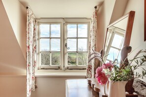 Ein Zimmer mit großem Fenster, blumigen Vorhängen und einer Vase mit Blumen.