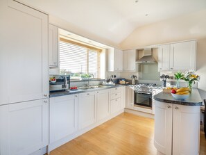 A modern kitchen with white cabinets, a granite countertop, and a wooden floor. - Branwen Cottage - UKC6122 (Pentraeth)