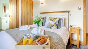 Ein ordentlich bezogenes Bett mit einem Frühstücksbrett, das Croissants und Orangensaft enthält, in einem Zimmer mit Holztüren und schlichtem, klarem Design.