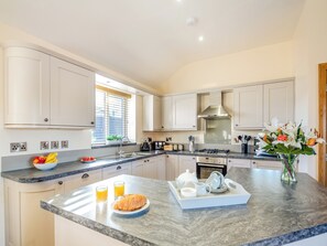 A modern kitchen with white cabinets, a granite countertop, and a breakfast tray with croissant, juice, and coffee. - Pwyll Cottage - UKC6123 (Pentraeth)