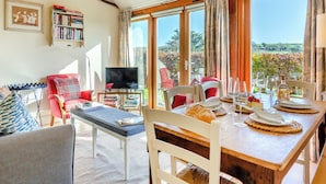 Uma sala de estar acolhedora com televisão, estantes de livros e um espaço de jantar com mesa posta para dois.