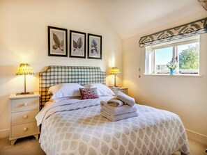 A neatly made bed with a checkered headboard, two bedside lamps, a window with a view of greenery, and three framed botanical prints on the wall. - Giddy Cottage - UKC6127 (East Dean)