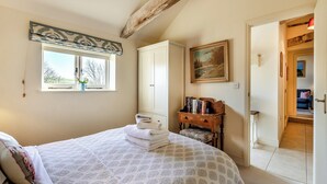 Ein Schlafzimmer mit einem Bett, einem Fenster, einem Gemälde und einem kleinen Holztisch mit Büchern.