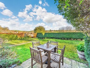 A patio with a wooden table and chairs, surrounded by a well-maintained lawn and hedges. - Giddy Cottage - UKC6127 (East Dean)