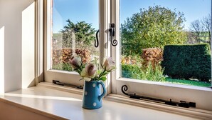 Ein Fenster mit Blick auf einen Garten, eine blaue, gepunktete Tasse auf der Fensterbank und eine schwarze Türklinke.