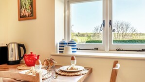 Ein Essbereich mit Holztisch, Wasserkocher, rotem Teekessel und Fenster mit Blick auf eine grüne Landschaft.