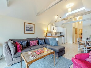 Ein modernes Wohnzimmer mit einem grauen Sofa, einem Holztisch und einem Essbereich mit einem weißen Tisch und Stühlen.
