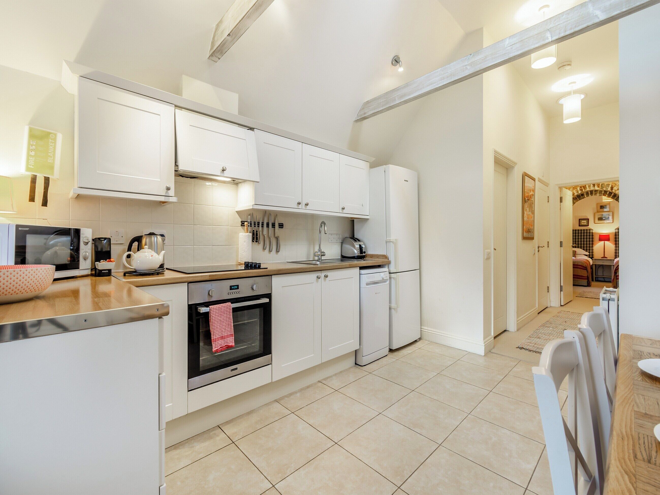 A modern kitchen with white cabinets, a built-in oven, a dishwasher, and a coffee maker.