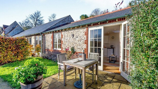 Una casa de piedra con un patio, una mesa de madera y una silla.