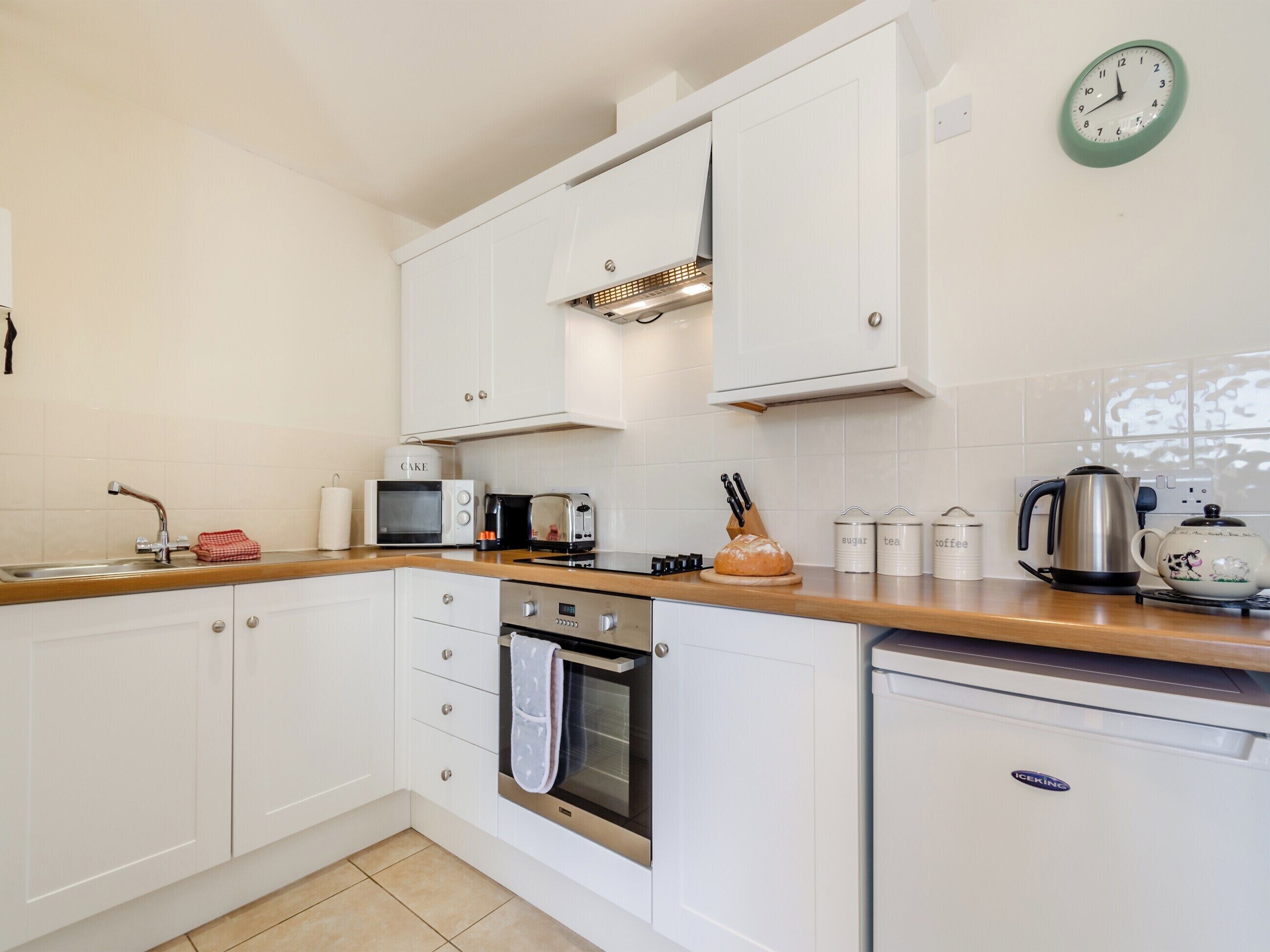 A modern kitchen with white cabinets, a microwave, toaster, kettle, and a clock on the wall.