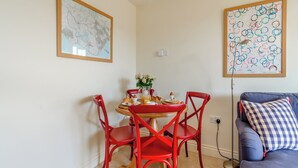 Un área de comedor con una mesa redonda, sillas rojas y un sofá azul con un cojín a cuadros.