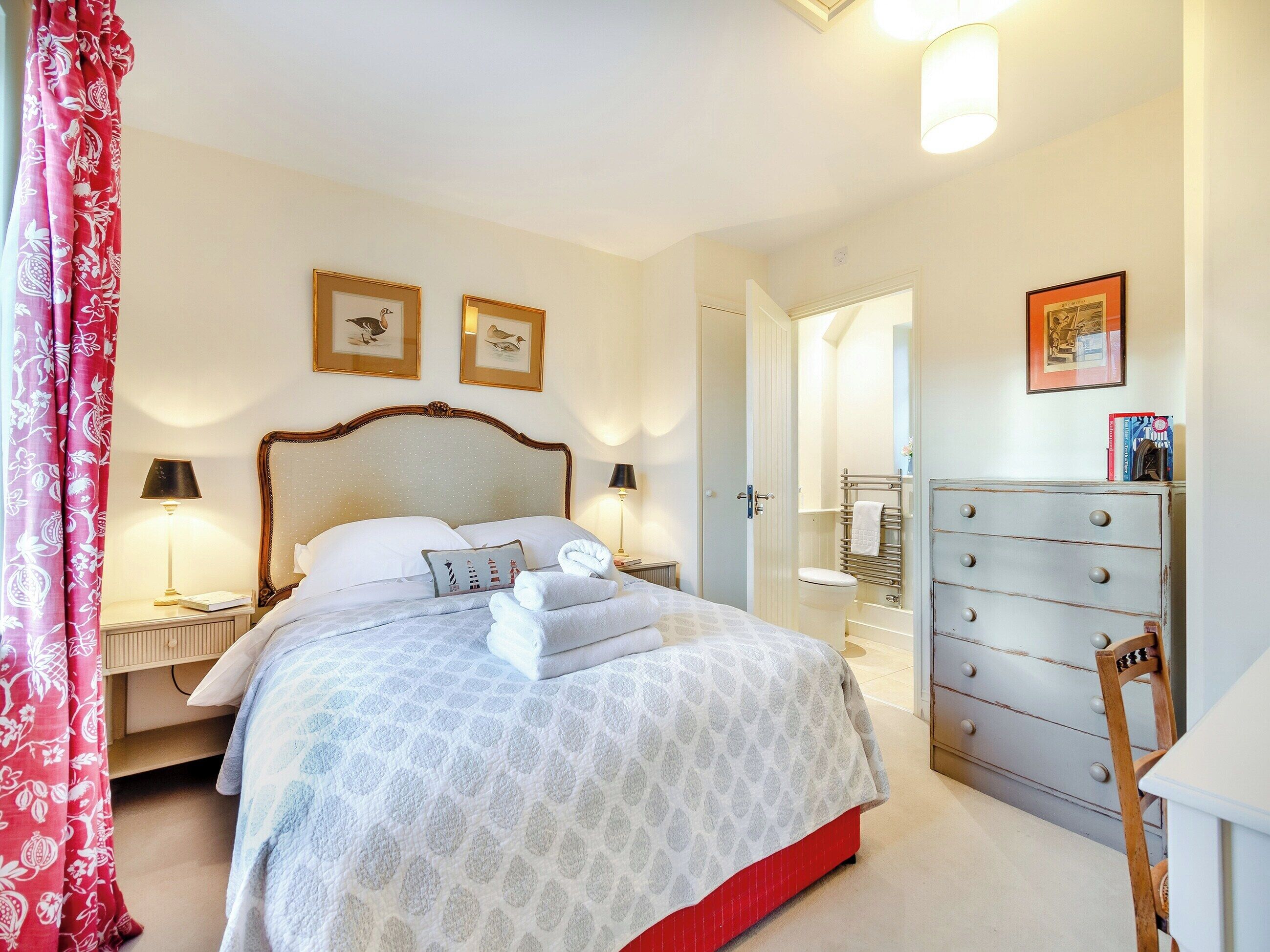 Un lit bien fait, avec des oreillers, une table de chevet avec une lampe, une commode et une porte donnant sur une salle de bain.