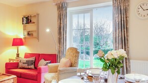 Ein gemütliches Wohnzimmer mit einem roten Sofa, einem Esstisch für zwei Personen und Blick ins Freie durch große Fenster.