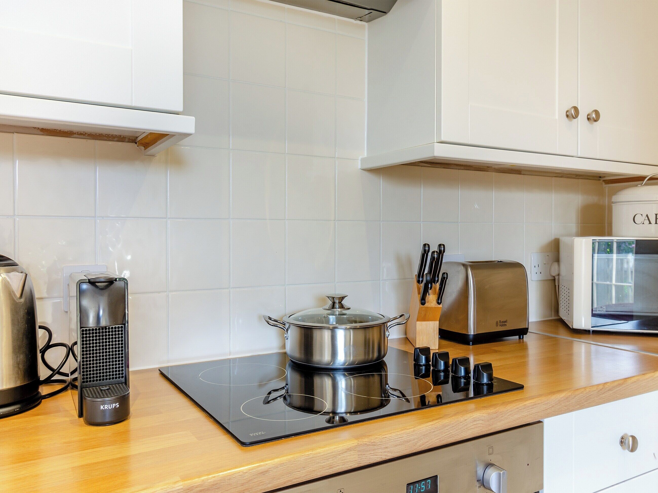 Una cocina moderna con placa de inducción integrada, tetera, tostadora y una olla en la hornilla.