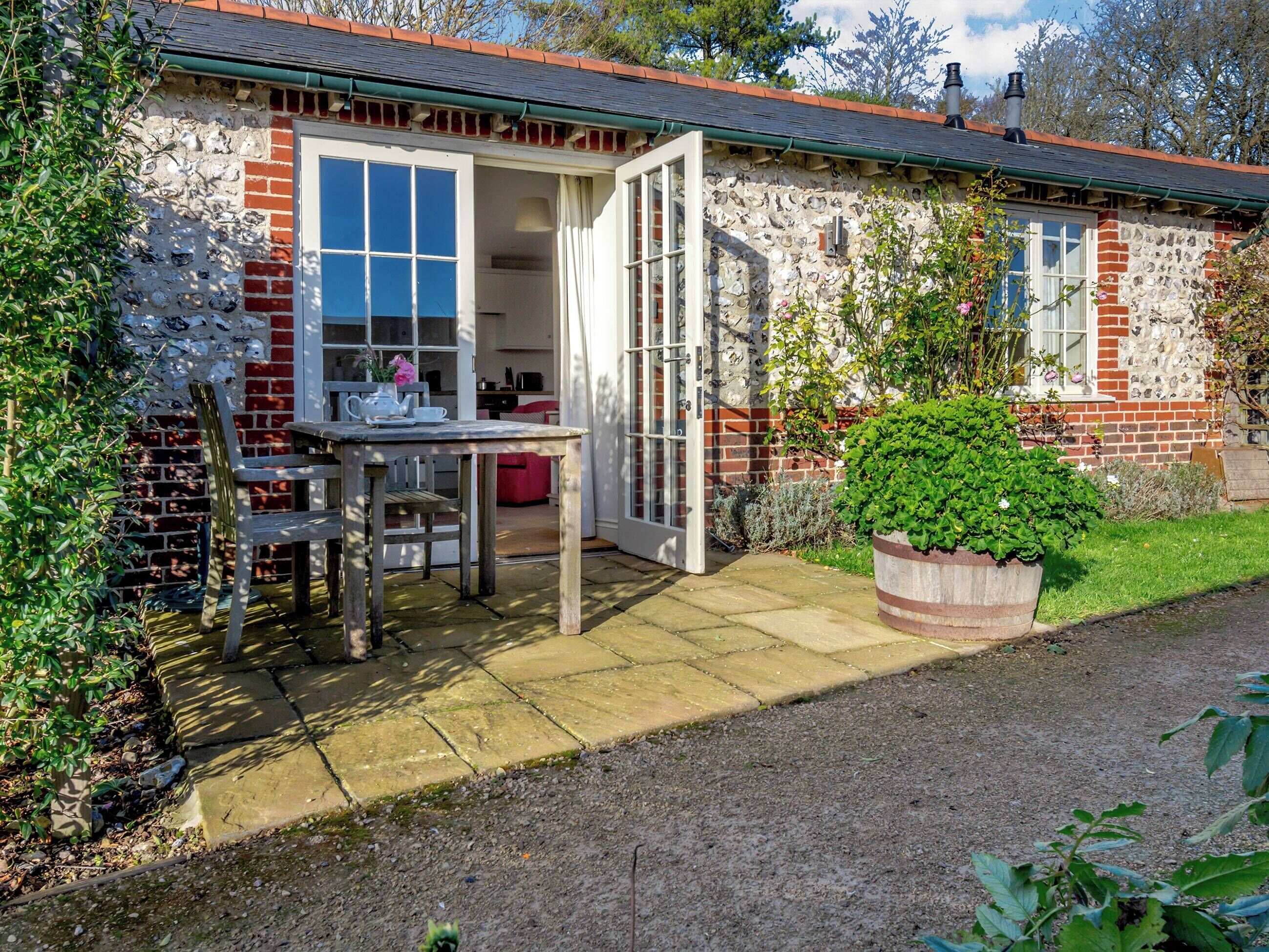 A stone house with a garden, a wooden table with chairs, and a potted plant.