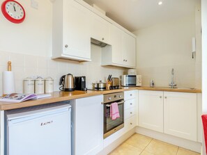 A modern kitchen with white cabinets, a stainless steel kettle, a microwave, and a sink.