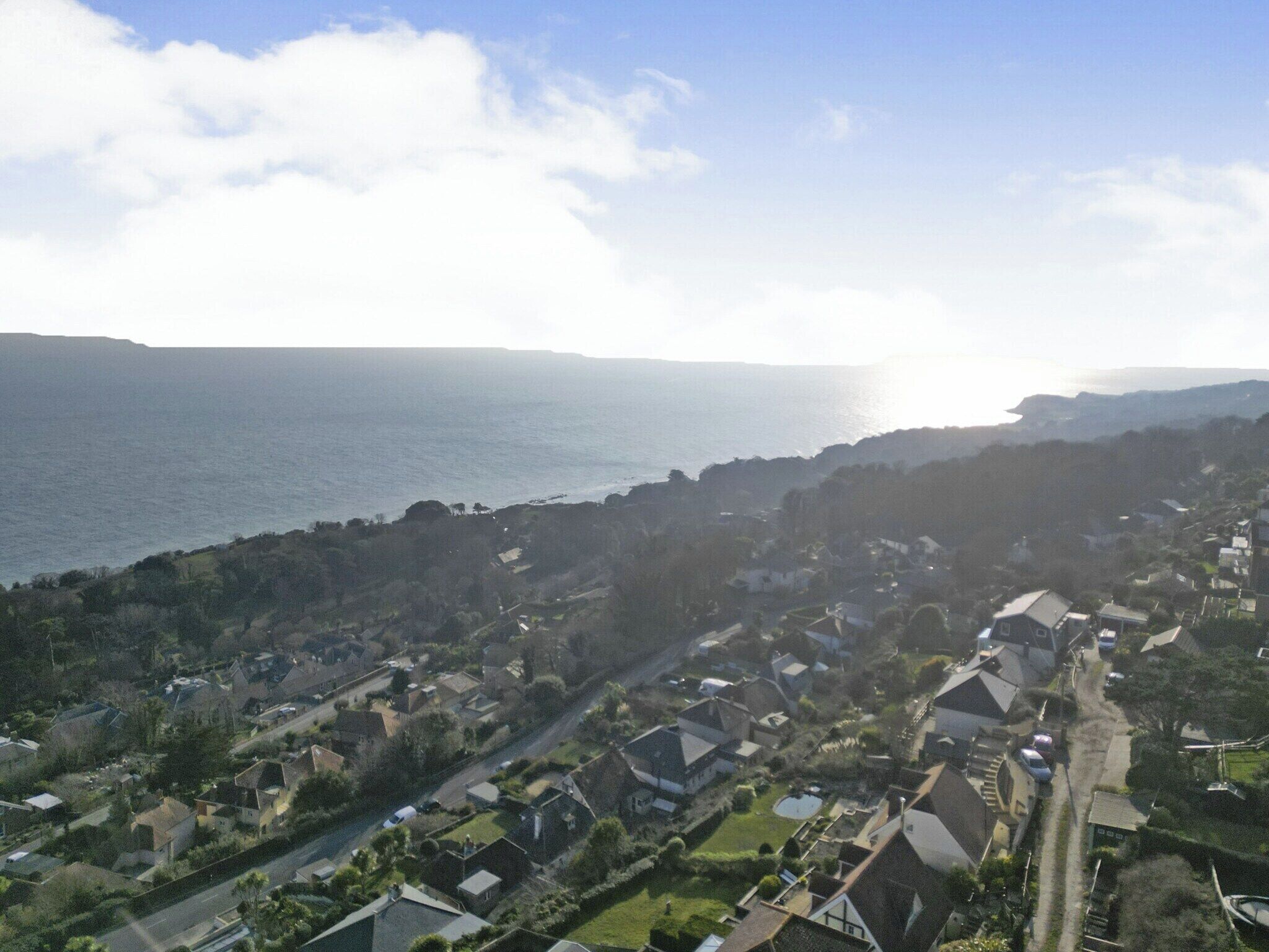 A coastal residential area with houses, a road, and a view of the sea.