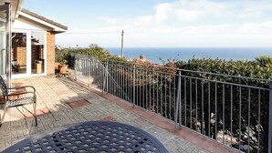 Un patio con una mesa y sillas de metal, un muro de ladrillo y vista al océano.