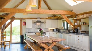 Een rustieke keuken met houten balken, een grote houten tafel en uitzicht op het landschap.