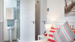 A hotel room with a bed, a bedside table with a lamp, a bathroom with a sink and glass shower enclosure. - Mermaids View - UKC6166 (Paignton)