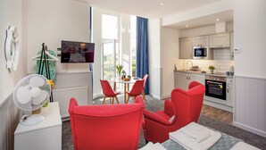 A modern apartment with a dining area, kitchen, and a living room with red chairs. - Mermaids View - UKC6166 (Paignton)