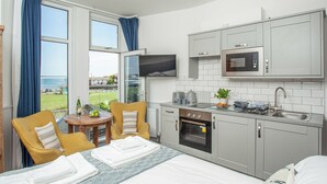 A modern kitchen with a built-in oven and microwave, a dining area with a table and chairs, and a large window offering a view of the sea. - The Little Lobster - UKC6167 (Paignton)