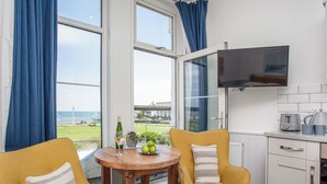A room with two yellow chairs, a wooden table, a bottle of wine, and a bowl of green apples. - The Little Lobster - UKC6167 (Paignton)