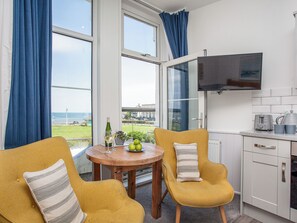 Ein Zimmer mit zwei gelben Stühlen, einem Holztisch, einer Weinflasche und einer Schüssel grüner Äpfel.