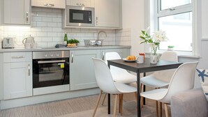 Una cocina moderna con armarios blancos, microondas, horno y comedor con mesa y sillas.