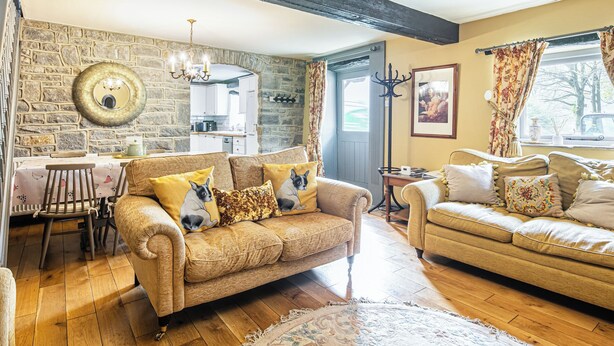 A cozy living room with a stone wall, wooden floor, and two sofas with patterned cushions. - 3 bedroom accommodation in Over Haddon, near Bakewell (Over Haddon, near Bakewell)