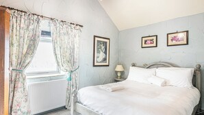 A bedroom with a bed, floral curtains, a radiator, a nightstand with a lamp, and framed pictures on the wall. - 3 bedroom accommodation in Over Haddon, near Bakewell (Over Haddon, near Bakewell)
