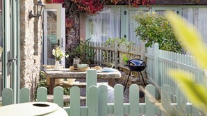 Een stenen gebouw met een houten terras, een tafel met buitenplaatsing, een barbecue en een witte picket fence.