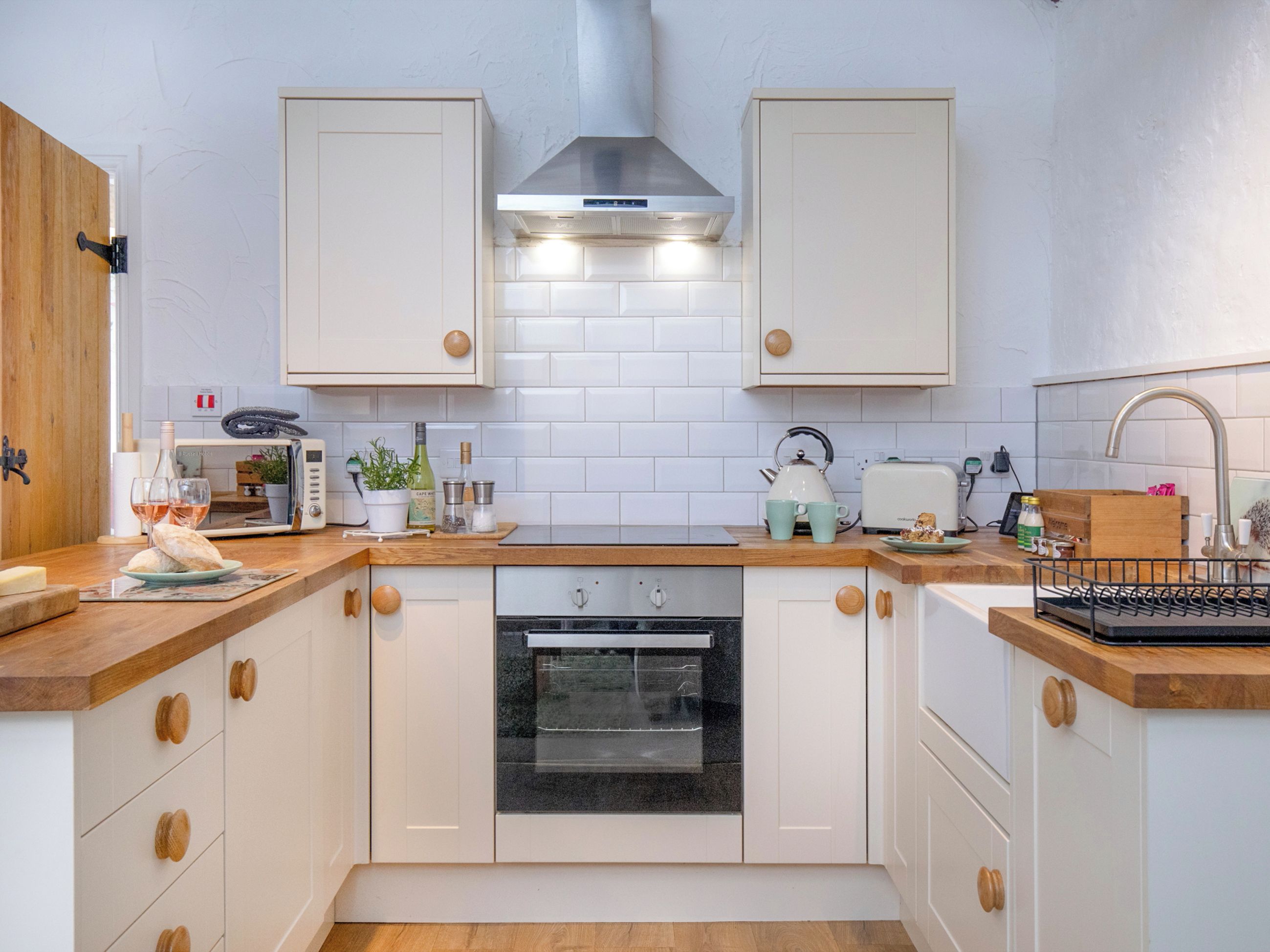 A kitchen with white cabinets, a stainless steel range hood, a built-in oven, and a wooden countertop.