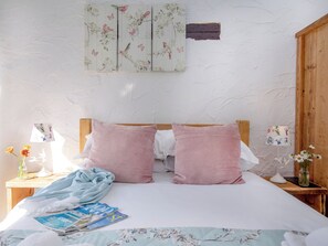 A bedroom with a wooden headboard, two pink pillows, a floral bedspread, a bedside table with a lamp, and a wall-mounted artwork. - Daisy Cottage - UKC6177 (Marldon, near Paignton)