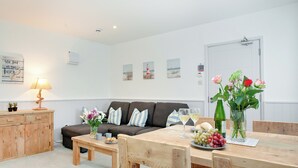 A well-lit living room with a wooden table set for dining, a sofa with striped cushions, and a wooden cabinet. - Anchors Away - UKC6170 (Paignton)