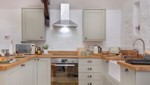A compact kitchen with white cabinets, a stainless steel range hood, a built-in oven, and a wooden countertop. - Jasmine Cottage - UKC6179 (Marldon, near Paignton)