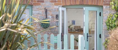 A stone building with a green door, a small garden, and a white picket fence.