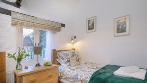 Ein Schlafzimmer mit einem hölzernen Bett, einem Nachttisch mit Lampe, einer Kommode und einem Fenster mit Blick auf Grünflächen.