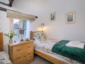 A bedroom with a wooden bed, a bedside table with a lamp, a dresser, and a window with a view of greenery. - Rose Cottage - UKC6181 (Marldon, near Paignton)