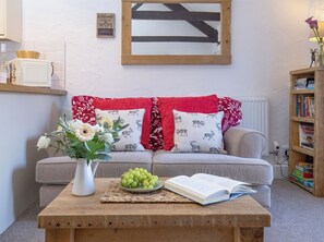A cozy living room with a sofa, a coffee table with a book and grapes, a vase with flowers, and a bookshelf. - Rose Cottage - UKC6181 (Marldon, near Paignton)