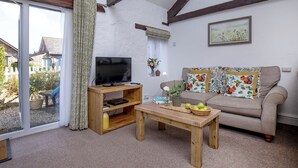 Ein Wohnzimmer mit Fernseher, Couch und Couchtisch aus Holz sowie Kissen mit Muster.
