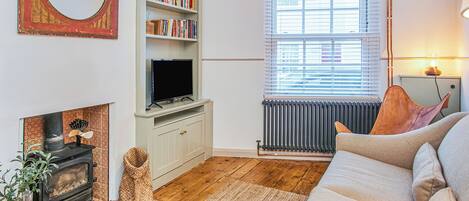 A living room with a fireplace, a bookshelf, a television, a sofa, and a window with blinds.