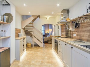 Una cocina moderna con una isla central, electrodomésticos integrados y una escalera de madera que lleva a un comedor.