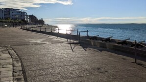 En strandpromenad med en gångväg av sten, bänkar och ett räcke med utsikt över havet.