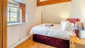 Un dormitorio con cama, ventana, radiador y viga de techo de madera.